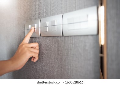 Close Up Of Finger Is Turning On Or Off On Light Switch Over Grey Wall At The Hotel. Copy Space.