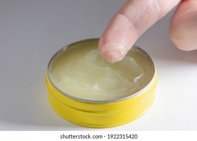 Close up of finger and yellow jar with vaseline balm on white background. There is vaseline on the finger and it can be used as lip balm or lubrication for sexual activities. 