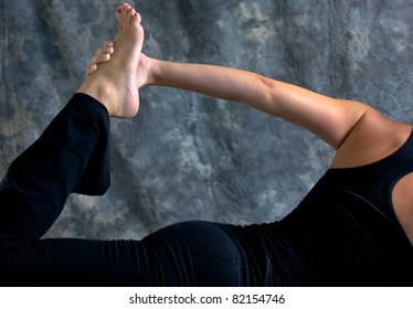 Close up of fit athletic woman doing half bow yoga pose showing arm and leg with hand holding foot in studio against a mottled background.