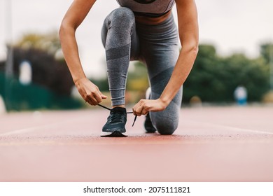 Close up of fit runner kneeling on the track in the stadium and tying shoelace on her sneaker. She is getting ready for training. A runner tying shoelace. - Powered by Shutterstock