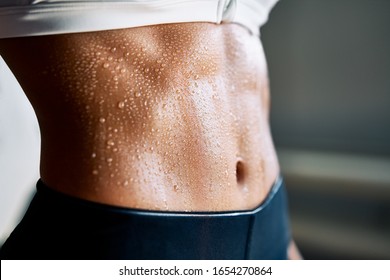 Close up of fit woman torso with sweat on skin after workout. Female with perfect abdomen muscles
