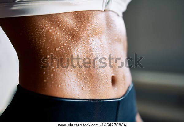 Close up of fit woman torso with\
sweat on skin after workout. Female with perfect abdomen\
muscles