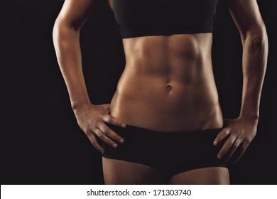 Close up of fit woman's torso with her hands on hips. Female with perfect abdomen muscles on black background