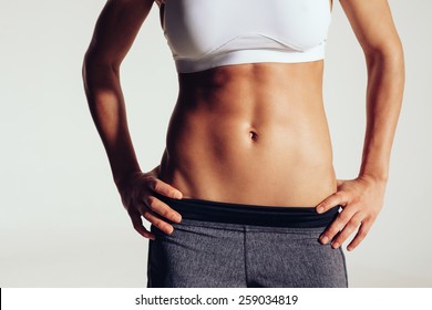 Close up of fit woman's torso with her hands on hips. Female with perfect abdomen muscles on grey background