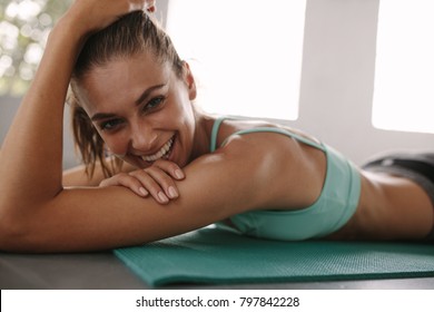 Close up of fit young female lying on exercise mat in gym and smiling. Healthy woman taking break after workout in gym. - Powered by Shutterstock