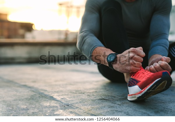 Close\
up of a fitness man tying lace of his sports shoes. Athlete getting\
ready for workout wearing shoes sitting on\
floor.