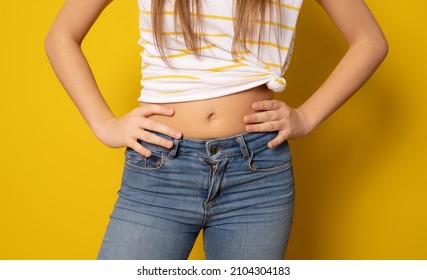 Close Up Of Flat Abdomen Of Young Woman In Ripped Jeans Isolated Over Yellow Background.