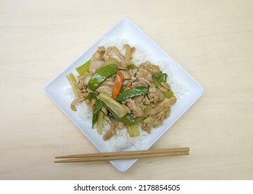 Close Up Flat Lay Top View Of A Square Plate With Almond Chicken Over Rice On A Wood Table With Chop Sticks On The Plate.