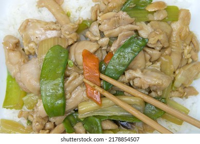 Close Up Flat Lay Top View Of A Square Plate With Almond Chicken Over Rice On With Chop Sticks Holding Carrot Slice.