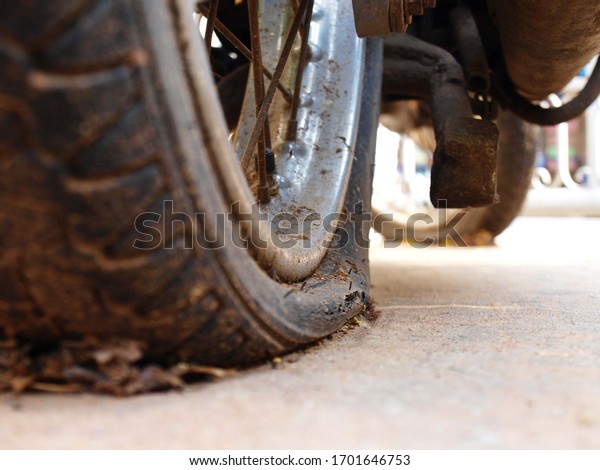 Close up the flat motorcycle tire with old rims.\
The motorcycle tire is dirty and cracked on the cement ground.\
Selective focus