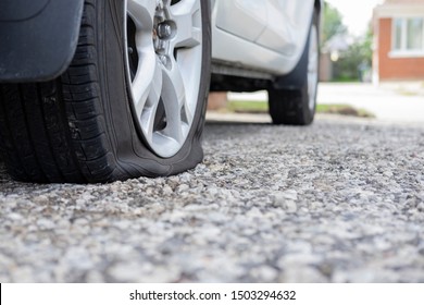 Close up of flat rear tire of white suv track car vehicle automobile punctured by nail. Summer day, residential street. Selective focus, depth of field, space for copy. Bad luck, accident concept.