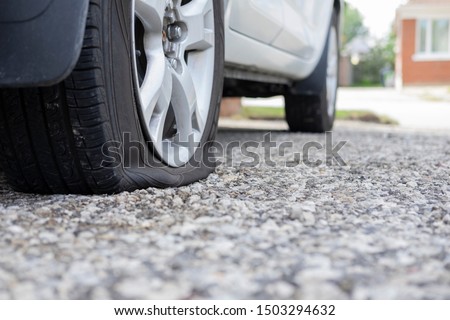 Close up of flat rear tire of white suv track car vehicle automobile punctured by nail. Summer day, residential street. Selective focus, depth of field, space for copy. Bad luck, accident concept.