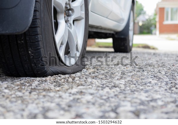 Close up of flat rear tire of white suv track\
car vehicle automobile punctured by nail. Summer day, residential\
street. Selective focus, depth of field, space for copy. Bad luck,\
accident concept.