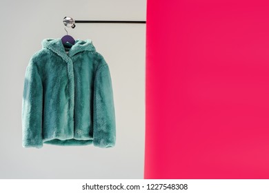 Close Up Of Fluffy Green Faux Fur Coat On Hanger With Pink Wallpaper 