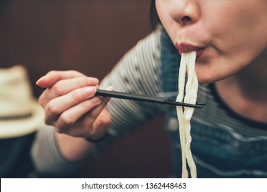 Close Up Focus Asian Woman Using Chopsticks To Clip The Noodles Into Mouth. Young Female Japanese Eating Having Lunch Taste Delicious Udon Ramen In Osaka Japan. Indoor Restaurant Concept Lifestyle.