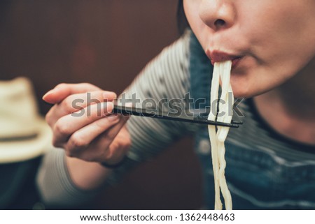 Close up focus Asian woman using chopsticks to clip the noodles into mouth. young female japanese eating having lunch taste delicious udon ramen in osaka japan. indoor restaurant concept lifestyle.
