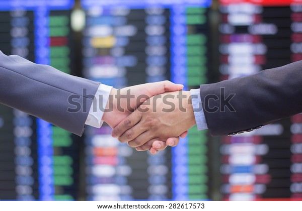 close up focus business man handshake on\
blurred stock trade board\
background