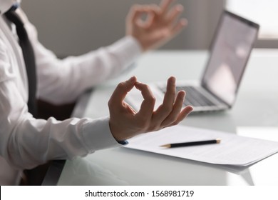 Close Up Focus Of Calm Businessman Sit At Office Desk Meditate During Work Day With Mudra Hands, Relaxed Male Employee Practice Yoga Control Relieve Emotions, Stress Free, Healthy Lifestyle Concept