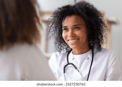 Close up focus on African smiling woman doctor in white coat stethoscope on neck look at patient listen examine health. Adolescent medicine hebiatrics or paediatrics, healthcare medical worker concept - Powered by Shutterstock