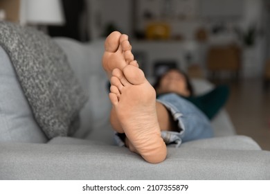 Close up focus on bare feet of relaxed young female homeowner fallen asleep on comfortable sofa in own apartment. Millennial tenant resting barefoot on cozy couch, pedicure procedure concept.