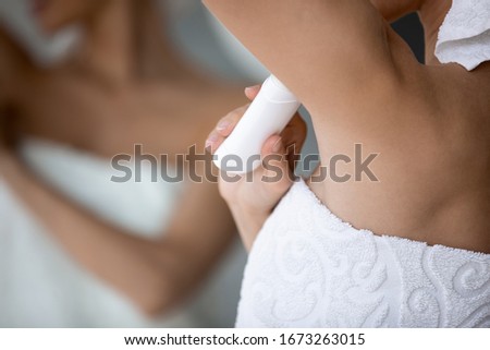 Close up focus on deodorant, applied under arm. Young woman preventing sweating in hot summer weather, using antiperspirant stick after taking shower, morning healthcare routine in bathroom.