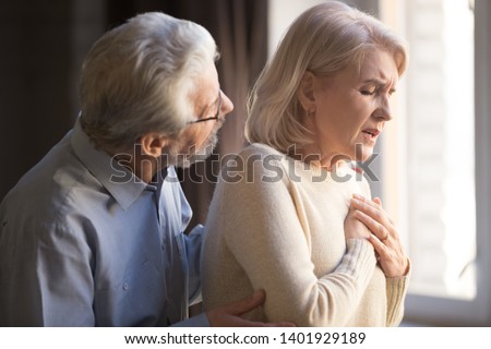 Close up focus on elderly wife hold hand on breast touch chest having heart attack feels unwell, worried husband supporting her, myocardial infarction symptoms, immediately emergency call need concept