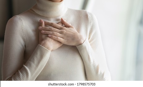 Close up focus on female hands, folded on chest. Happy young woman employee feeling thankful indoors, praying for good luck on important business meeting, dreaming of future, appreciation concept.