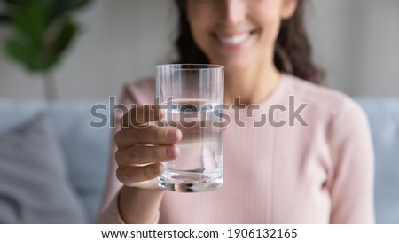 Close up focus on glass with mineral clean water in female hands. Happy sincere young woman showing fresh pure aqua to camera, recommending daily organism hydration norm, healthcare habit concept.