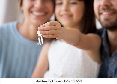 Close up focus on hand of little girl holding keys. Happy family married couple wife and husband and preschool daughter move relocate at new home, buy first property dwelling mortgage and loan concept