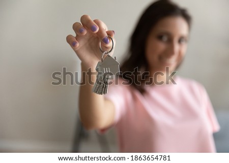 Close up focus on keys with cute house shape keychain in female hands, smiling mixed race arabic homeowner celebrating moving into new apartment, making bank mortgage credit deal real estate concept.