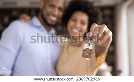 Close up focus on keys in hands of blurred joyful young loving african american married couple. Sincere mixed race homeowners celebrating purchasing own flat, feeling excited of renting new dwelling.