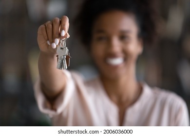 Close up focus on keys with keychain in African American young woman hand with blurred background, satisfied tenant renter excited by relocation, proud homeowner purchasing new apartment home