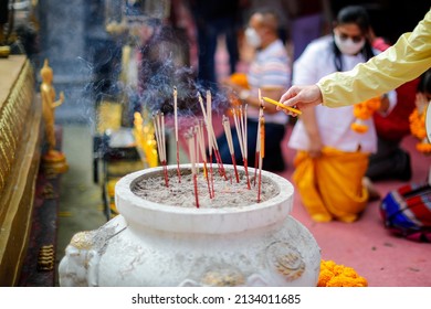 Close focus on lady hand light candle and incense on big jar with blurry background of unknown people come to worship buddha stupa inside sacred pagoda in Thailand. - Powered by Shutterstock