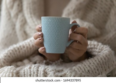 Close up focus on mug with hot beverage in wrinkled female hands. Middle aged elderly grandmother wrapped in knitted warm plaid holding cup with tea coffee, enjoying cozy weekend evening time alone. - Powered by Shutterstock
