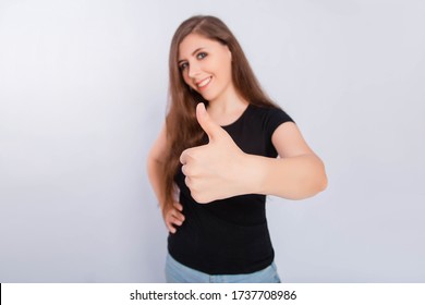 Close up focus on thumb up shot on wide angle lens. Young, attractive woman in a black t-shirt isolated on a white background shows a gesture of approval and success.