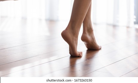 Close Up Focus On Young Female Feet Walking Barefoot On Clean Wooden Floor At Home. Cropped Image Millennial Woman Girl Standing On Warm Floor Without Slippers Indoors, Underfloor Heating Concept.