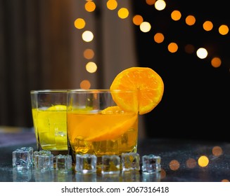 Close Up Focus At Slice Fresh Orange On Glass Rim, With Orange And Lemon Juice In Front Of Light Background, Bartender Prepare Fruit Cocktail Or Fresh Juice For Drinking In Party At Bar