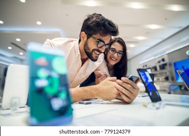 Close Up Focus View Of A Cheerful Charming Happy Young Student Love Couple Choosing A New Mobile In A Tech Store.