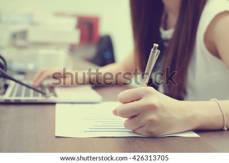 close up focus woman hand write on printout,type laptop computer in office room.