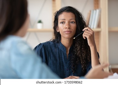 Close up focused african american businesswoman listening new female applicant. Serious diverse woman hr manager holding pencil looking at job seeker candidate in office at hire meeting.
