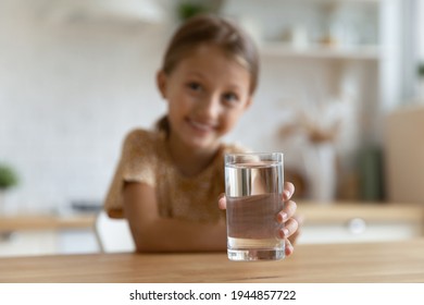 Close up focused blurred background of little happy girl hold glass of water recommend drink for body refreshment. Smiling kid child fell thirsty enjoy clean clear mineral aqua. Hydration concept.