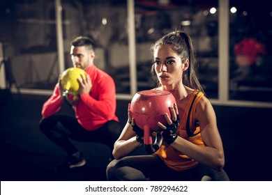 Close up of focused and motivated strong young fitness couple in sportswear crouching with the kettlebells reversed and doing squats in the gym. - Powered by Shutterstock