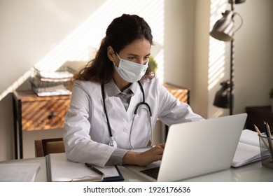 Close up focused professional female doctor physician wearing protective face mask using laptop, looking at screen, consulting patient online, chatting, browsing medical apps, searching information - Powered by Shutterstock