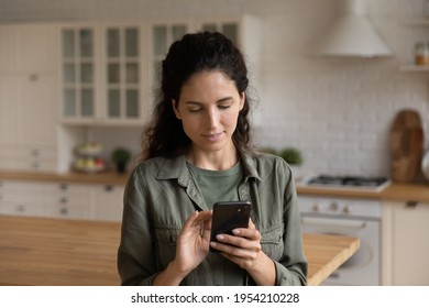 Close up focused woman looking at phone screen, browsing mobile device apps, standing in kitchen at home, confident young female typing, writing message, shopping or chatting online, scrolling - Powered by Shutterstock