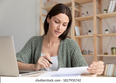 Close up focused young businesswoman working with documents in office, sitting at work table with laptop, serious employee checking financial report, project statistics, reading correspondence - Powered by Shutterstock