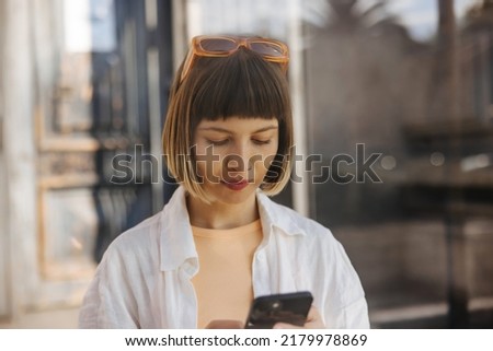 Close up focused young caucasian woman typing text on phone standing outdoors. Brown-haired with bob haircut and bangs wears shirt. Cell phone usage concept Stock photo © 