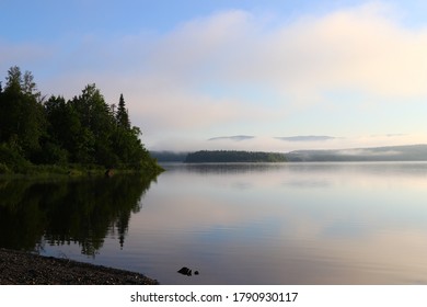 Close Up Of Foggy Treeline At Lakes Edge With Mountain In Mist