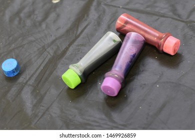 Close Up Of Food Coloring Dye Bottles Laying Down On Black Plastic Table Cloth Background