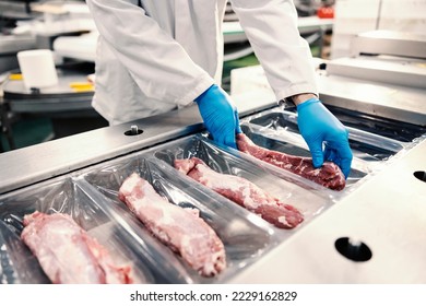 Close up of a food factory worker packing meat into the plastic on a packing machine. Expense of a meat. - Powered by Shutterstock