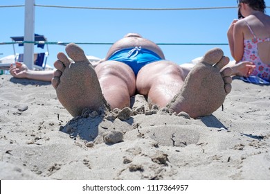 Close Up The Foot Of The Sunbathing Fat Man Photographed In A Comical Foreshortening